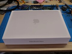 Pudełko detaliczne MacBooka Neo umieszczone na stole warsztatowym przed demontażem w celu modernizacji dysku SSD