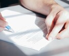 Ręka podpisuje dokument niebieskim długopisem
