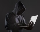 Zakapturzony haker obsługujący laptopa na ciemnym tle.