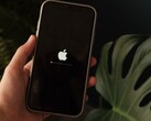 Ręka trzyma iPhone’a, a na ekranie widoczne są logo Apple oraz pasek postępu.